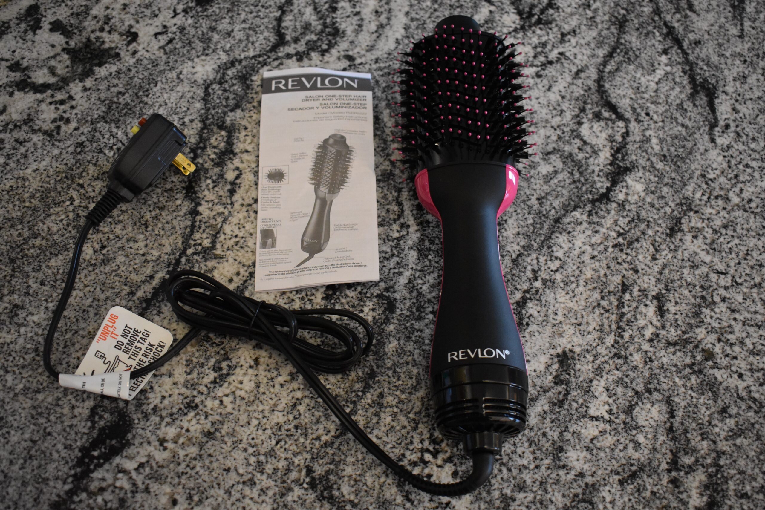 Revlon electric hair brush sits on the counter next to its cord and instructions