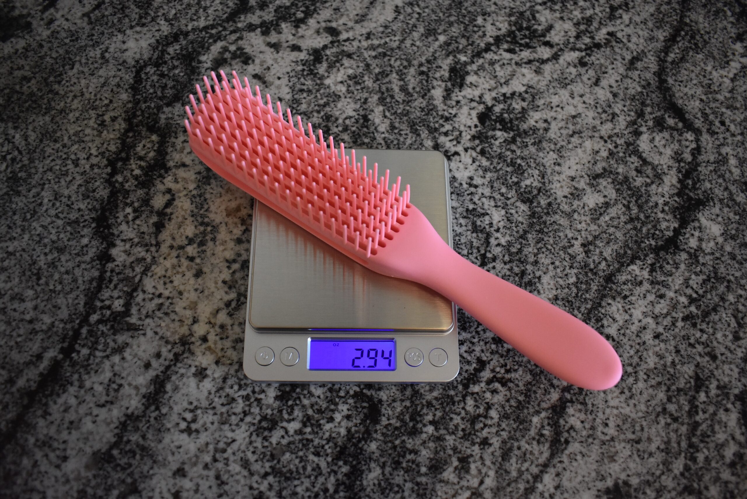 The best detangling brush in pink registering 2.94 oz on the scale on a granite counter