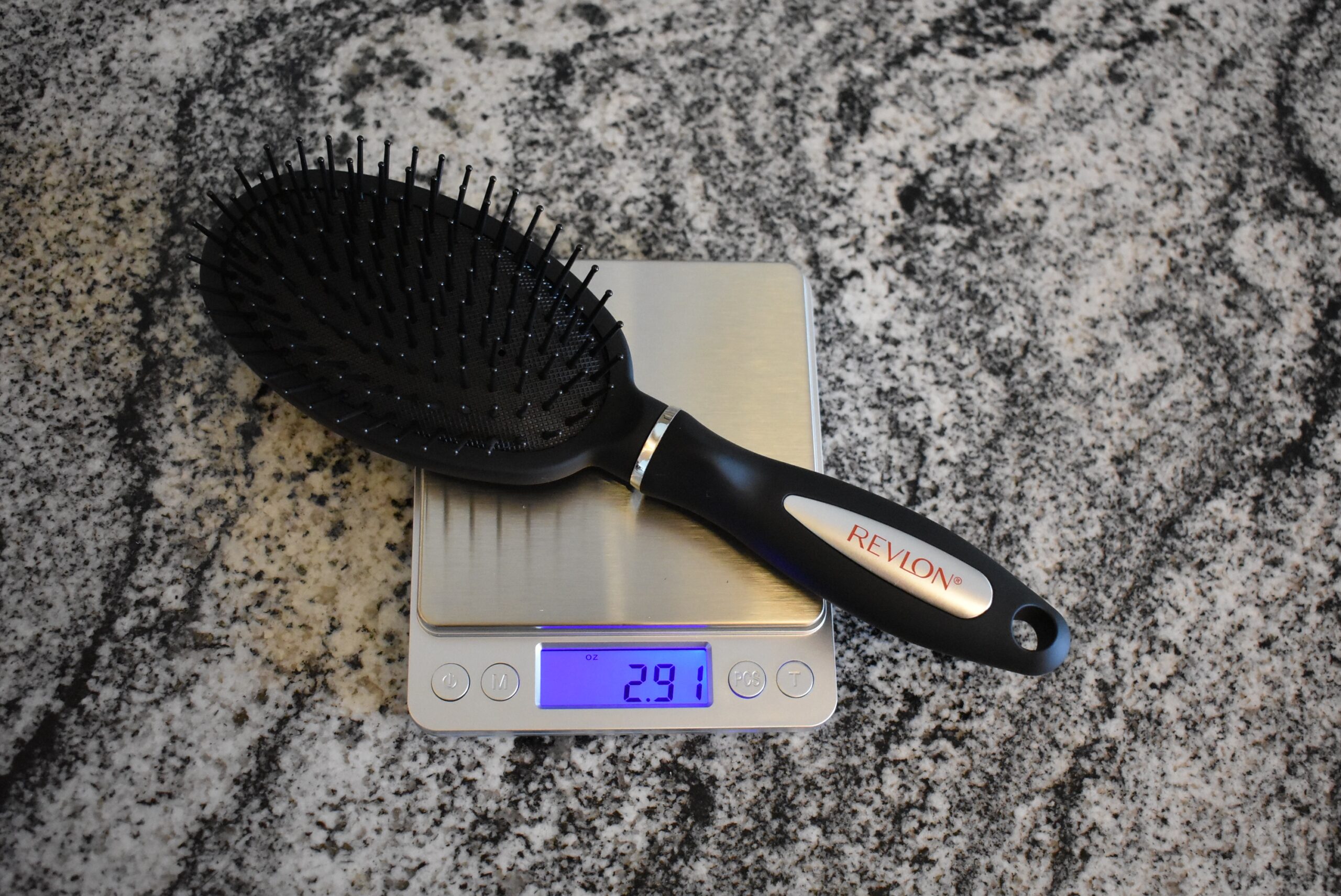 A Revlon hair brush sitting on a scale and registering 2.91 oz