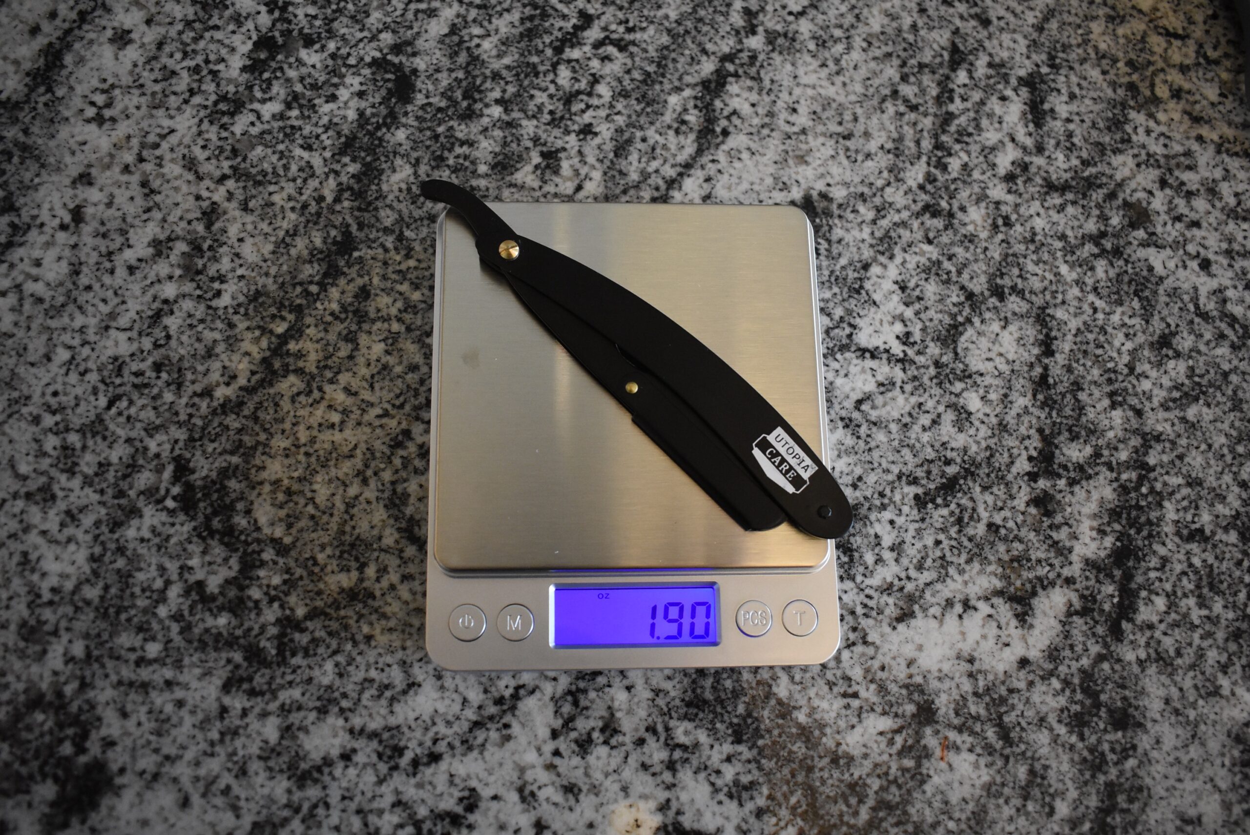Utopia Care straight razor sitting on a kitchen scale weighing 1.90 oz