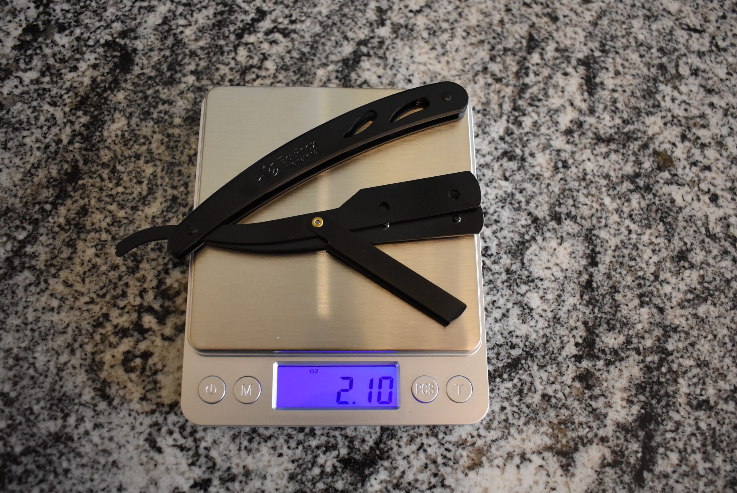 The Equinox professional straight razor showing 2.10 oz on a kitchen scale on a counter