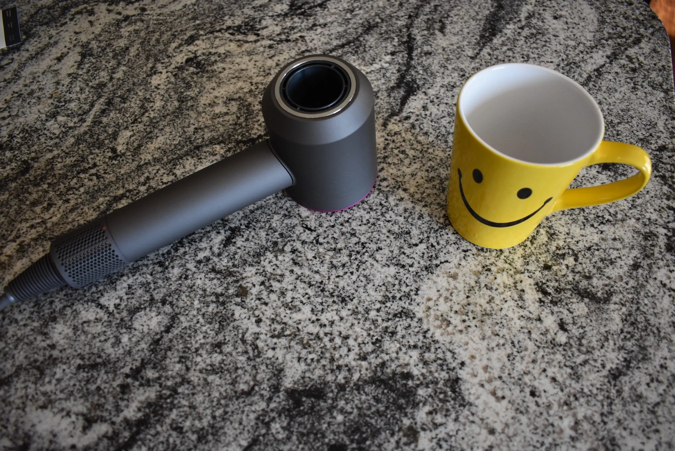 The dyson hair dryer sitting on a counter next to a yellow happy face mug