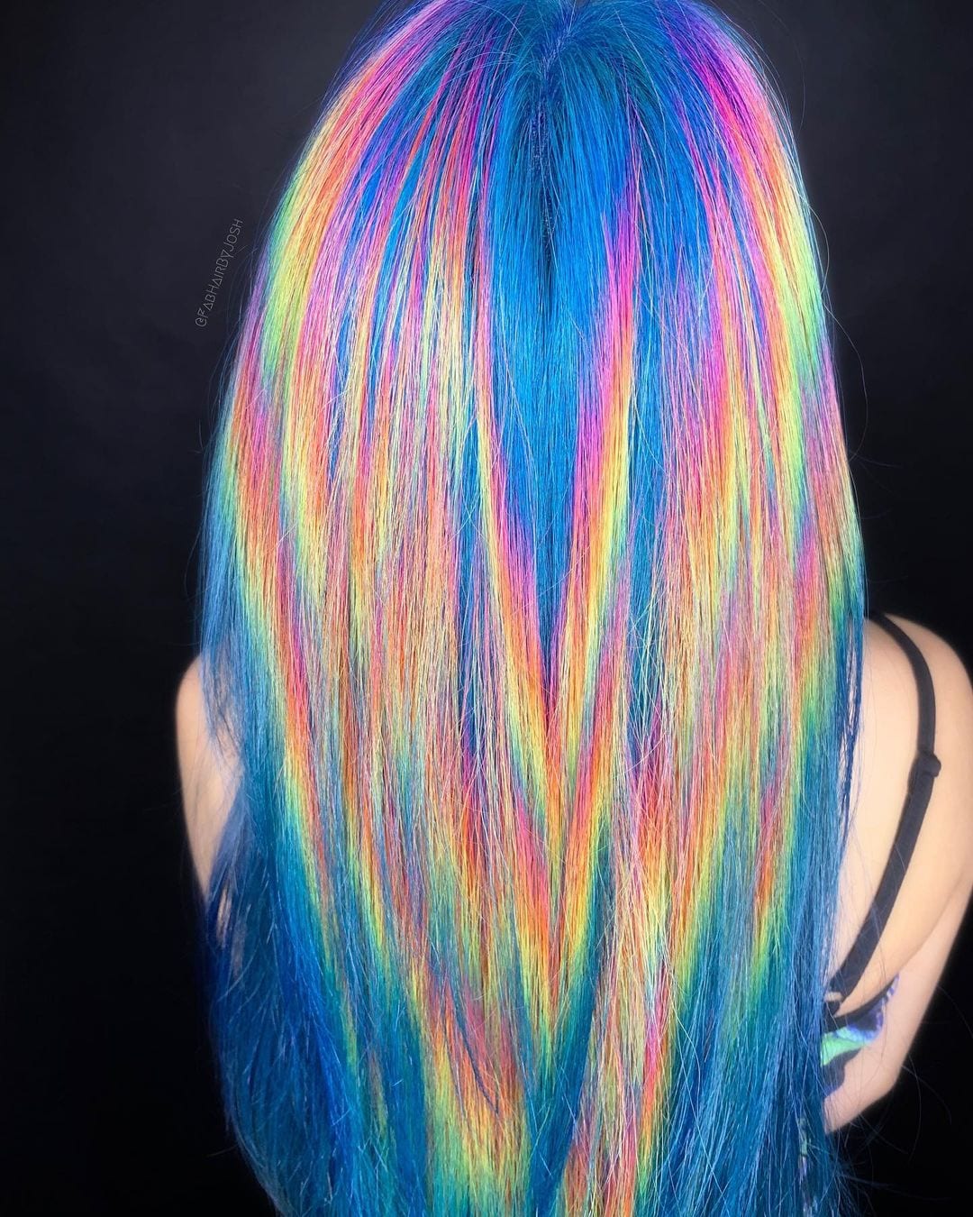 Holographic storm hairstyle on a blonde in a tie dye camisole standing away from the camera in a dark room