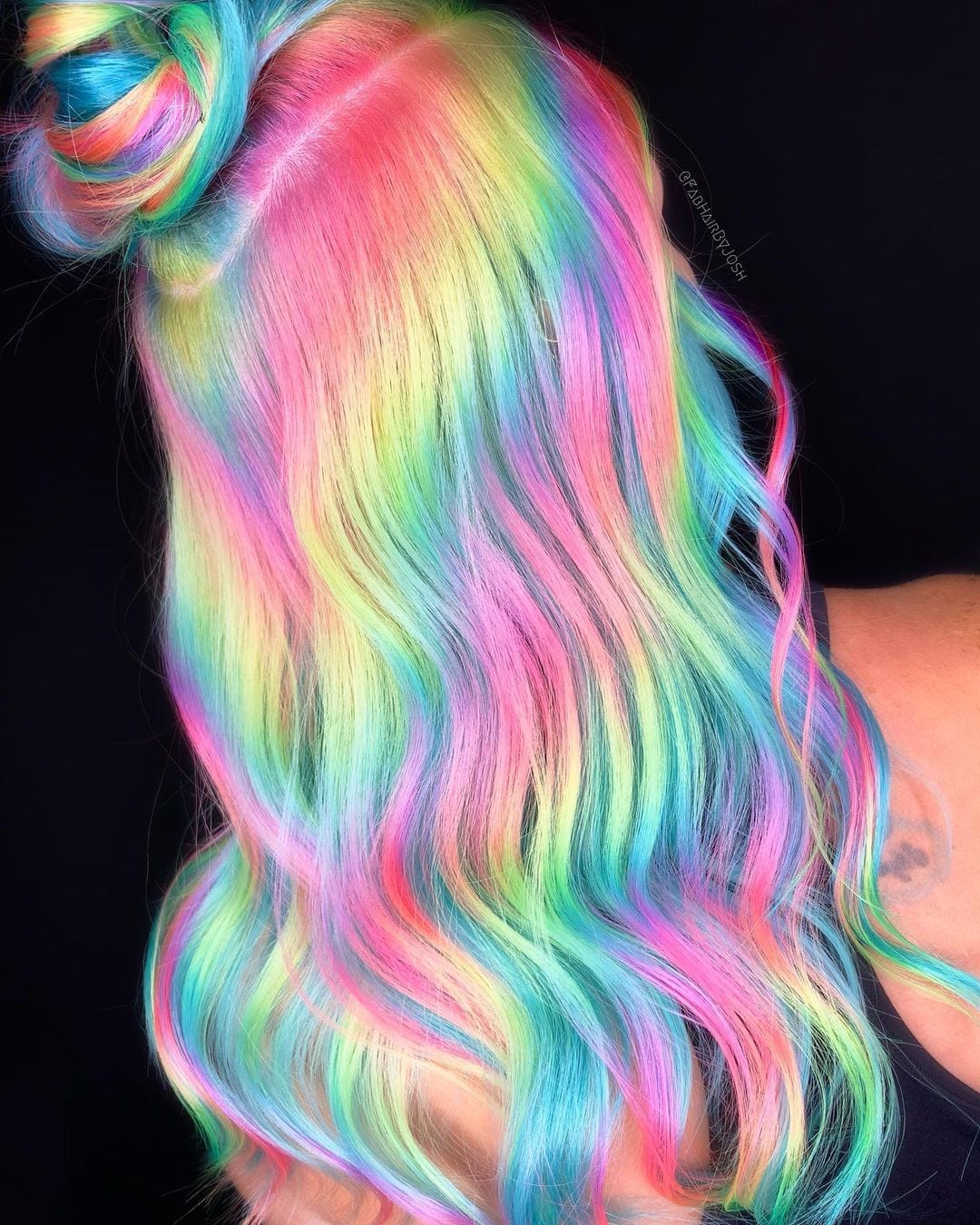 Candyland-esque holographic hair on a woman with a messy bun in a dark room