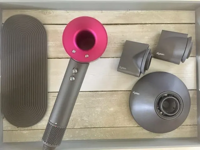 For a Dyson hair dryer review, the box contents including three attachments and a mat sit on a wooden cutting board