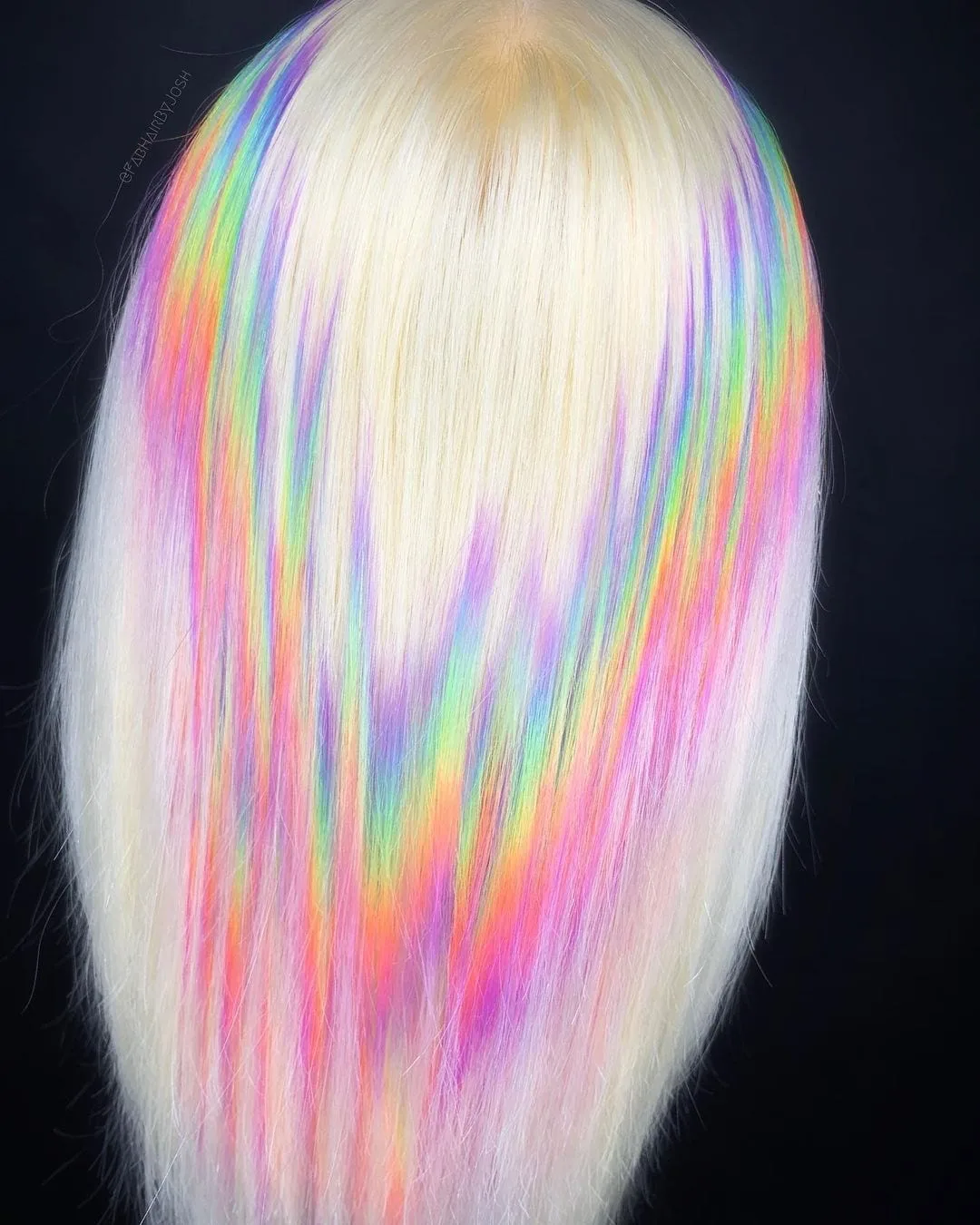 Jagged rainbow holographic hair on a blonde woman standing in a studio facing the black wall