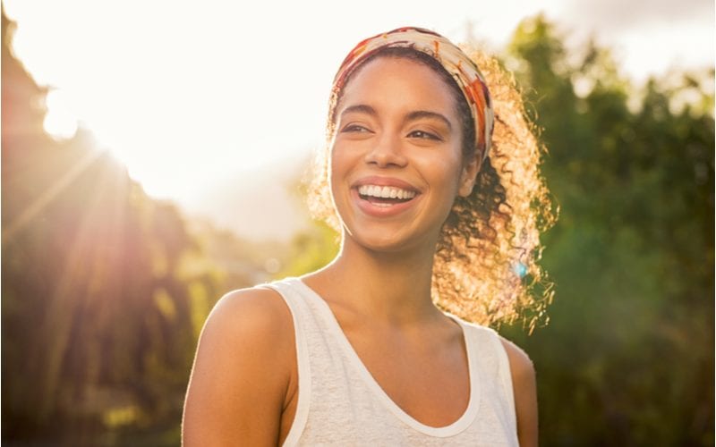 The wrapped headband, one of our favorite natural hairstyles, on a woman in a white tank top in a forest