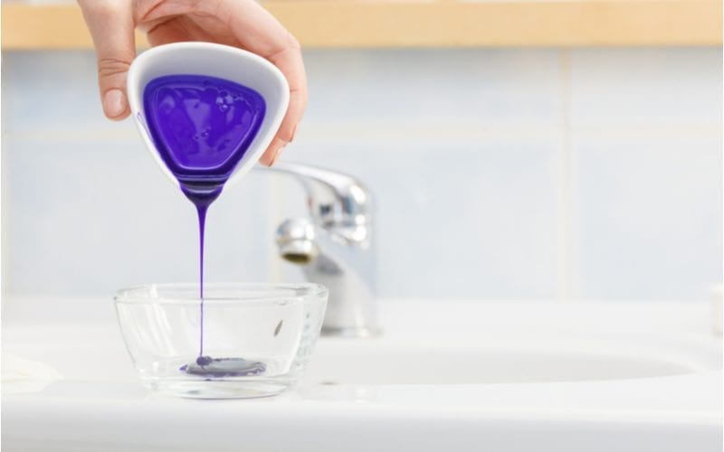 For a piece on what is hair toner, a woman pours a purple toner from a cup into a clear bowl