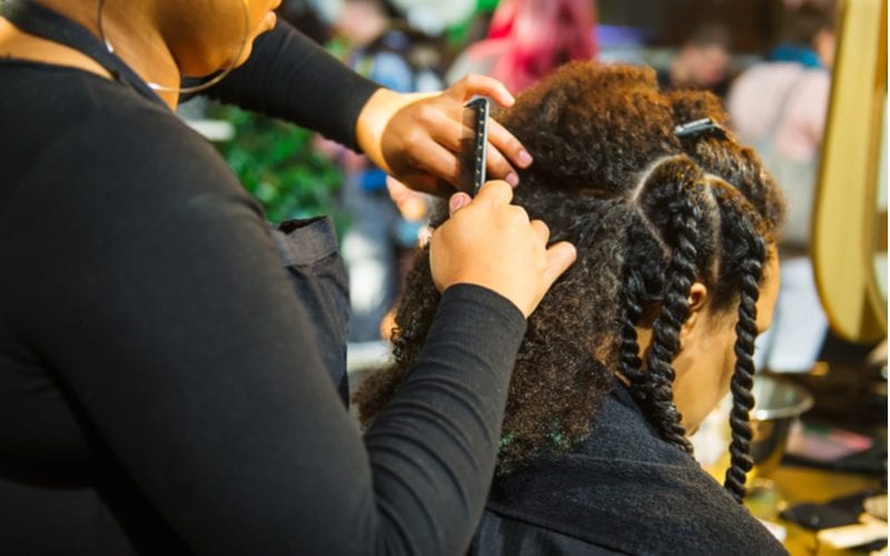 Woman in a natural hair style studio getting two-strand twists from a woman in a black shirt with hoop earrings