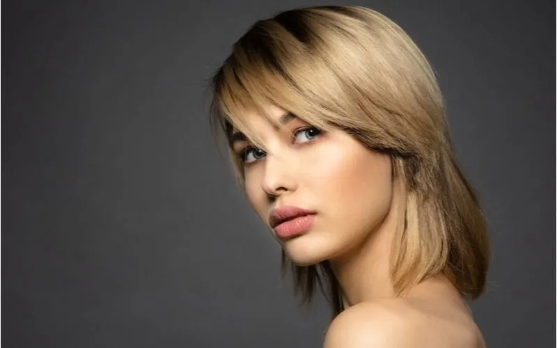 Blonde woman in a studio with a shoulder-length shag haircut that almost looks like a mullet