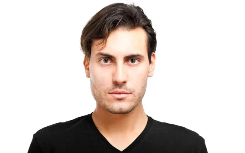 Guy in a black vneck with side-swept bangs and tapered sides in a studio stands against a white background