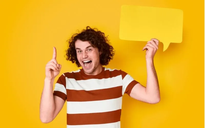 Guy holds up a sign that symbolizes the best hairstyles for wavy hair men while also holding up a 