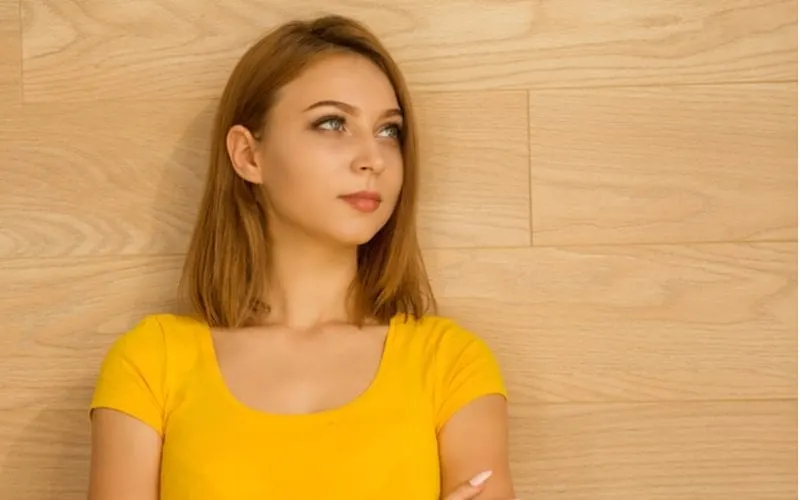 Young woman in a yellow top crossing her arms and looking up and to her right