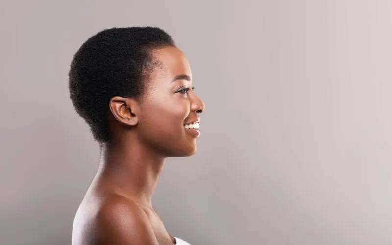 Woman with a natural hairstyle of shaved short hair stands in a side profile and smiles