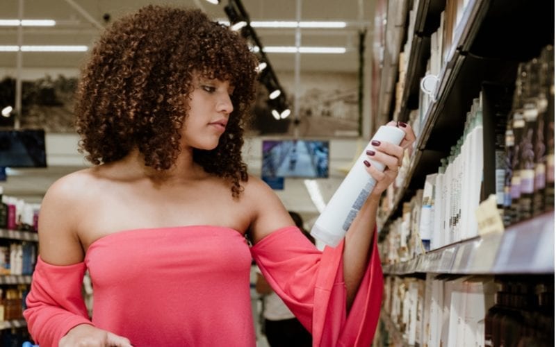 Happy young woman with naturally curly hair wears a tube top and looks at the best conditioner for sale in the supermarket