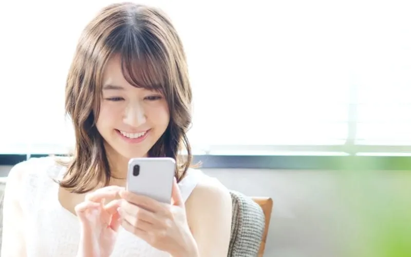 Young asian woman with a 60s shag lob holding her mobile phone and smiling at something she sees on the screen