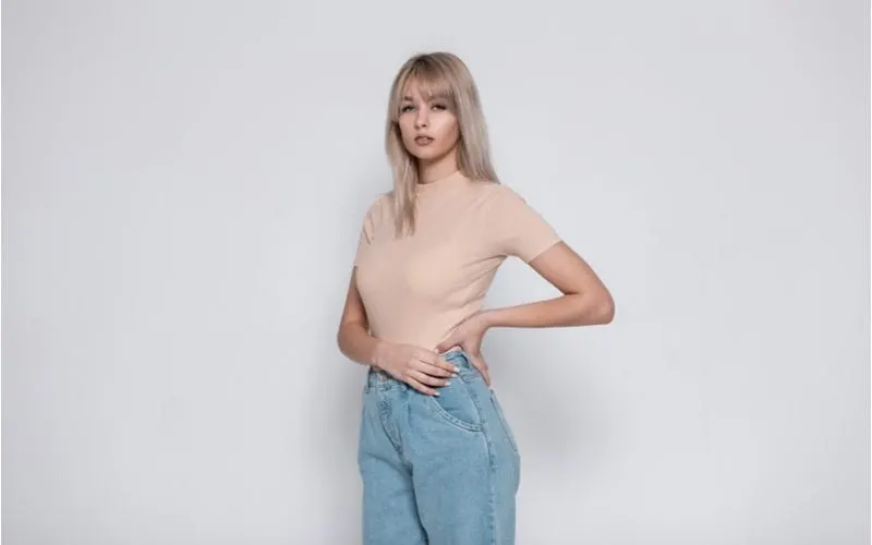 Fashionable woman with curtain bangs holds her hip in jeans