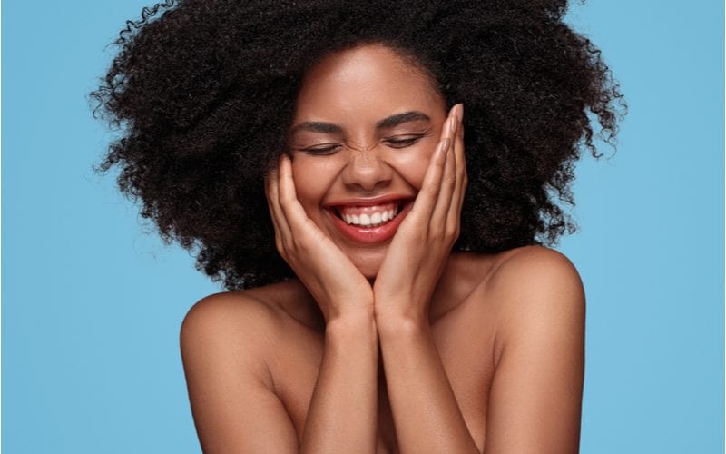 Young woman with natural hair holds her face and smiles