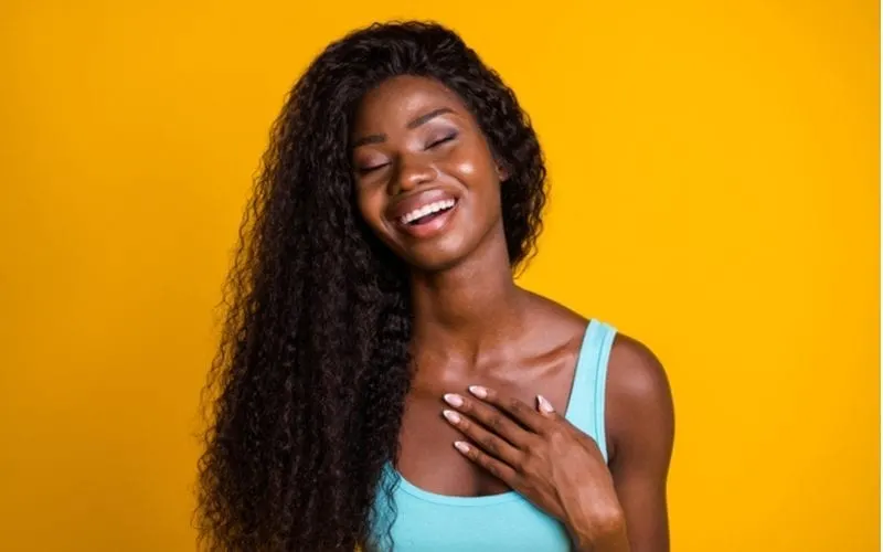 African american woman in a studio against an orange background wears a blue dress and lets her gorgeous curly hair flow