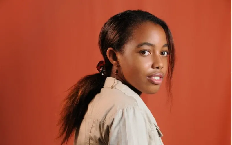 Natural hairstyle with a pressed pony on a woman in front of a red background