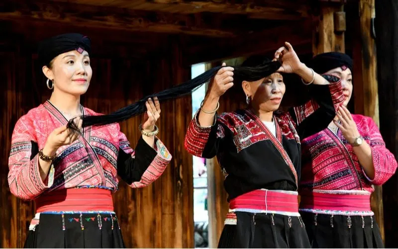 Image of three Red Yao women holding their hair up, as they only cut it once in their lifetime. They use rice water for their hair