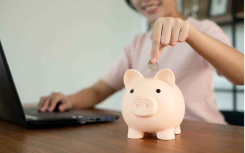 Woman putting a coin in a white piggy bank for a piece on Smartstyle Prices
