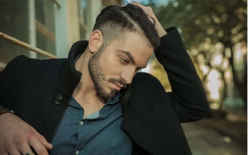 Image of a handsome man with a round face and a fade holding the top of his parted hair