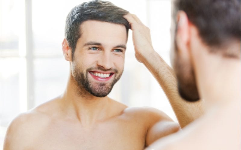 Shirtless man with a clean brushed-over taper haircut (best haircut for round faced men) smiles and gazes at himself