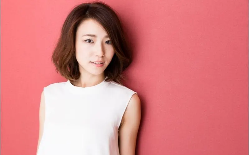 Fashionable young asian woman without makeup standing naturally against a dark pink wall with a long bob haircut