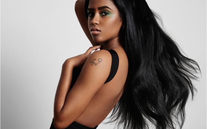 Young african american model with a long flowing black weave hairstyle holds her left arm to her neck