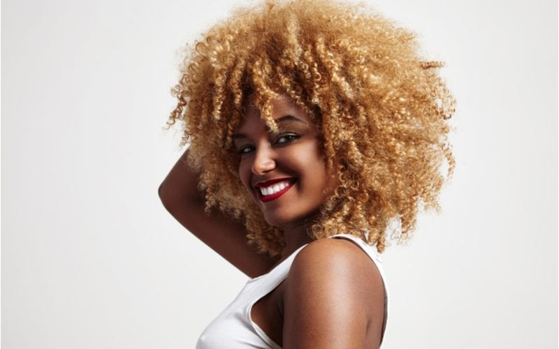 Braless woman with an afro and strawberry blonde hair holds her head with her right hand
