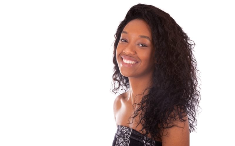 Gorgeous african american woman with a shoulder-length weave hairstyle stands in a studio and smiles