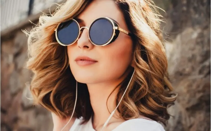 Woman in round hipster sunglasses stands outside a beach and wears sunglasses