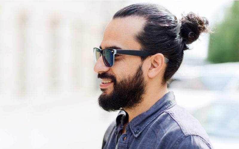 Guy in dark sunglasses with a beard and a man bun has one of our favorite haircuts for men with round faces
