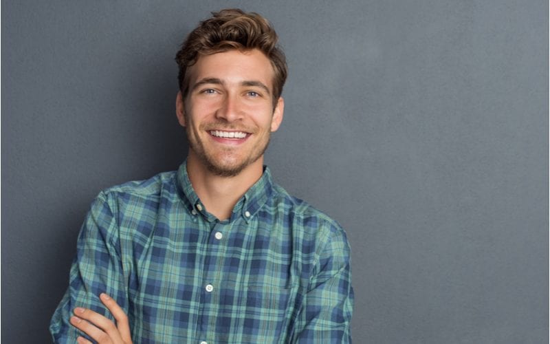 Handsome young wavy haired man crossing his arms while wearing a plaid button-up and smiling in a studio