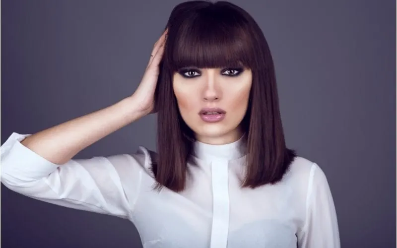 Pretty Russian woman with a long bob and very dark eyeliner holds the right side of her head