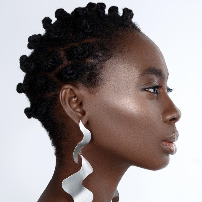 Side profile of a pretty young woman with Bantu Knots (a popular natural hairstyle) wearing long silver earrings