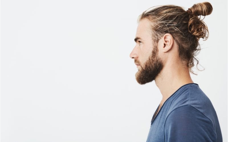 Side profile of a wavy hair man in a blue shirt standing in a studio on a white background