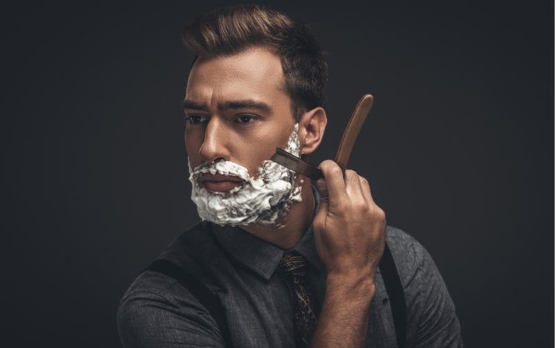 Man standing in front of the camera shaving with a straight razor
