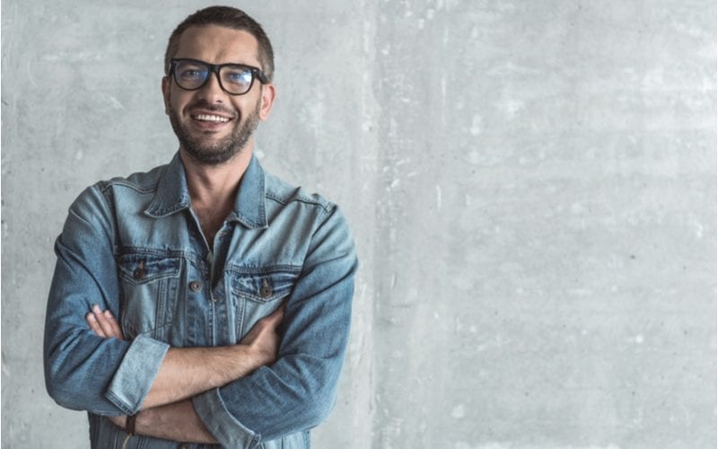 Round face man with a short buzz cut smiles and wears glasses while crossing his arms in a blue jean shirt