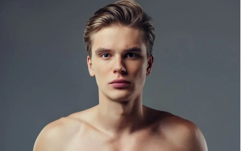 Round faced man wears no shirt and has a long brushed-back taper haircut and looks directly into the camera