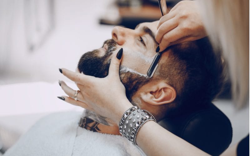 Guy with a beard getting a shave from the one of the best straight razors in a barbershop