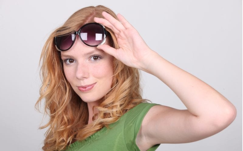 Woman with strawberry blonde hair holds sunglasses up onto her forehead