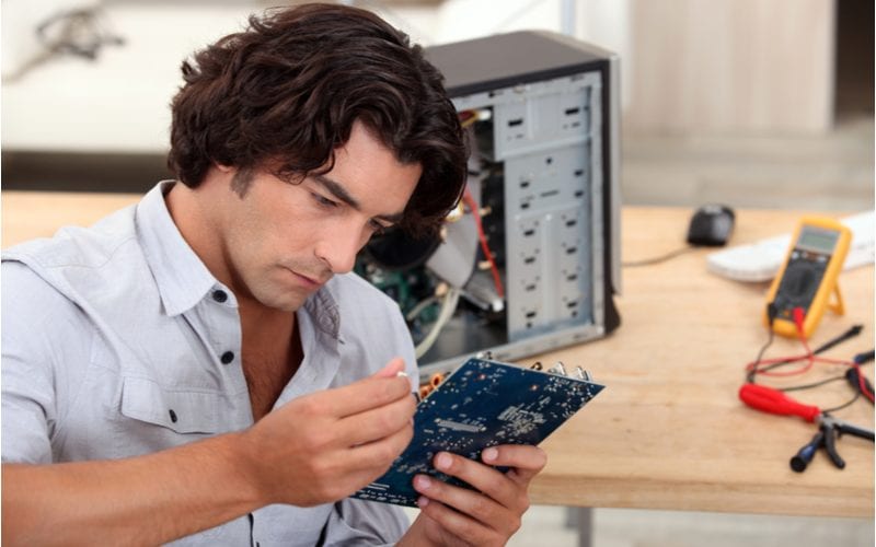 Young man with middle-parted long waves looks at a piece of computer hardware