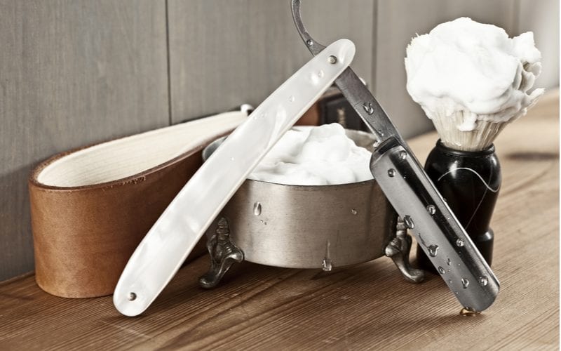 One of the top rated straight shavers sitting open on the counter next to a thing of beard oil and shaving cream