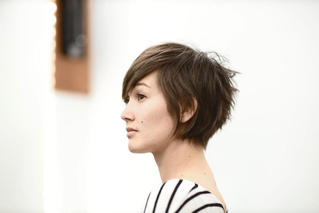 Woman with a slightly asian complexion and a pixie cut stands seriously contemplating life