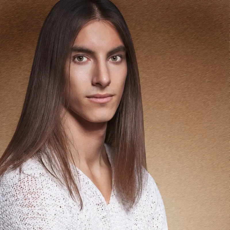 Man with shiny long hair that looks like he was in Nirvana stands crossing his arms in front of a speckled brown wall