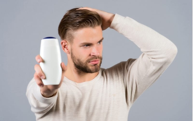 Man holding his head and in the other hand holding up a bottle of hair growth shampoo