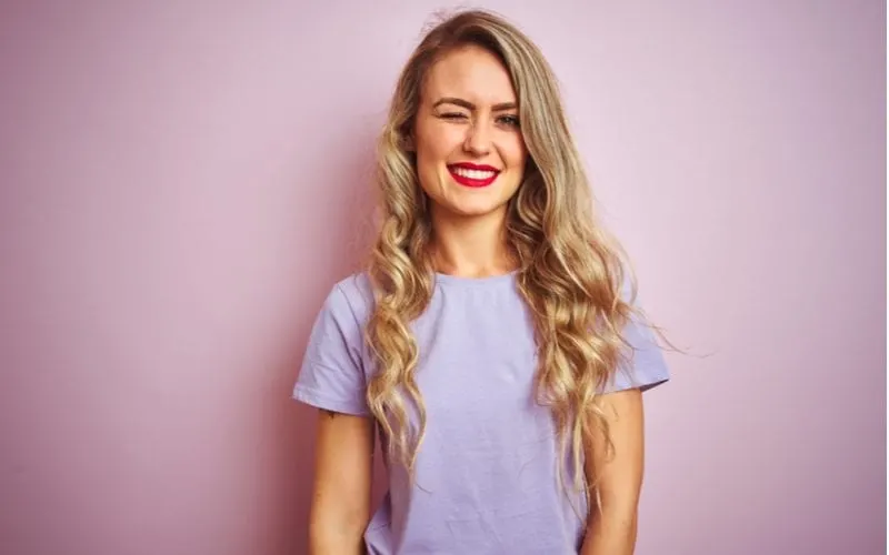 Young lady with a purple shirt standing in a purple room winking and wearing red lip