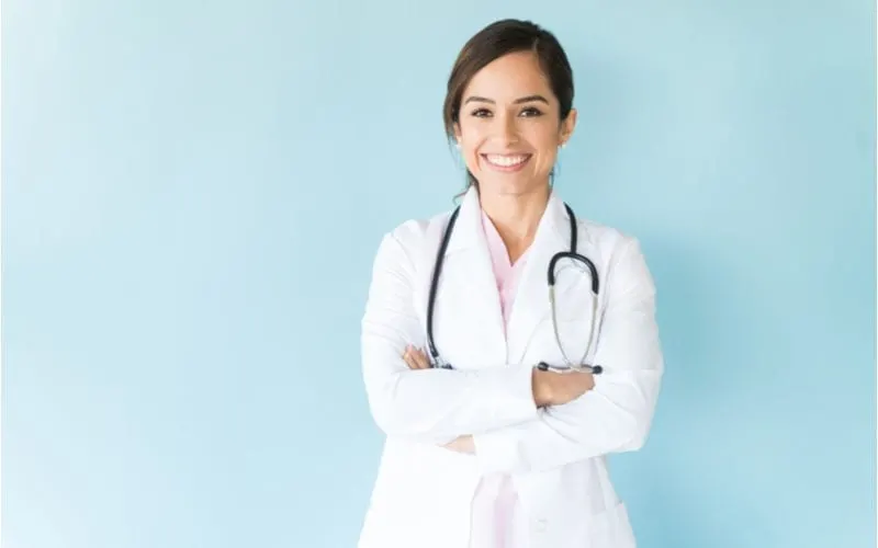 For a piece on what is an ingrown hair, a woman with a white coat and stethoscope stands against a blue wall